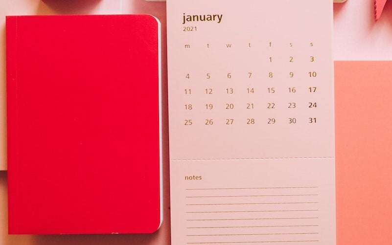 Flat lay of pink sheet with January month calendar and pink notepads with pins