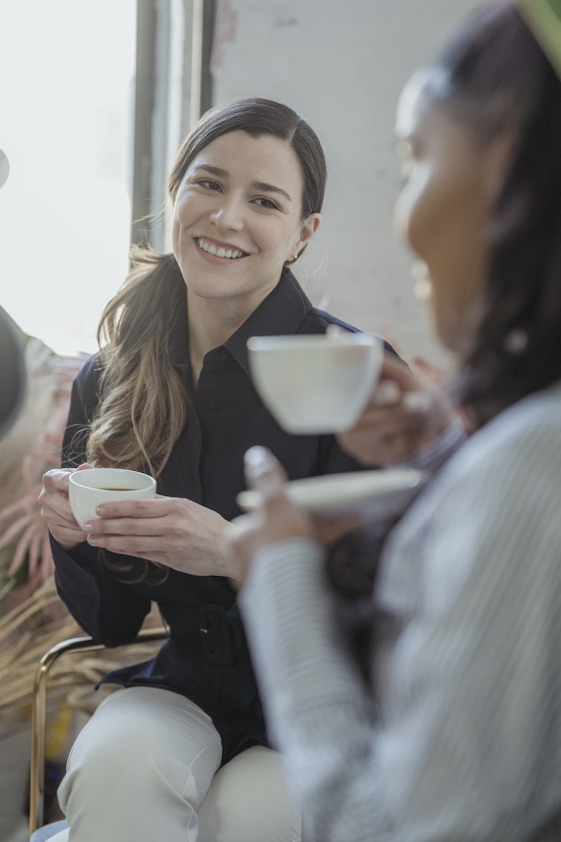 Positive diverse friends talking and having cup of coffee